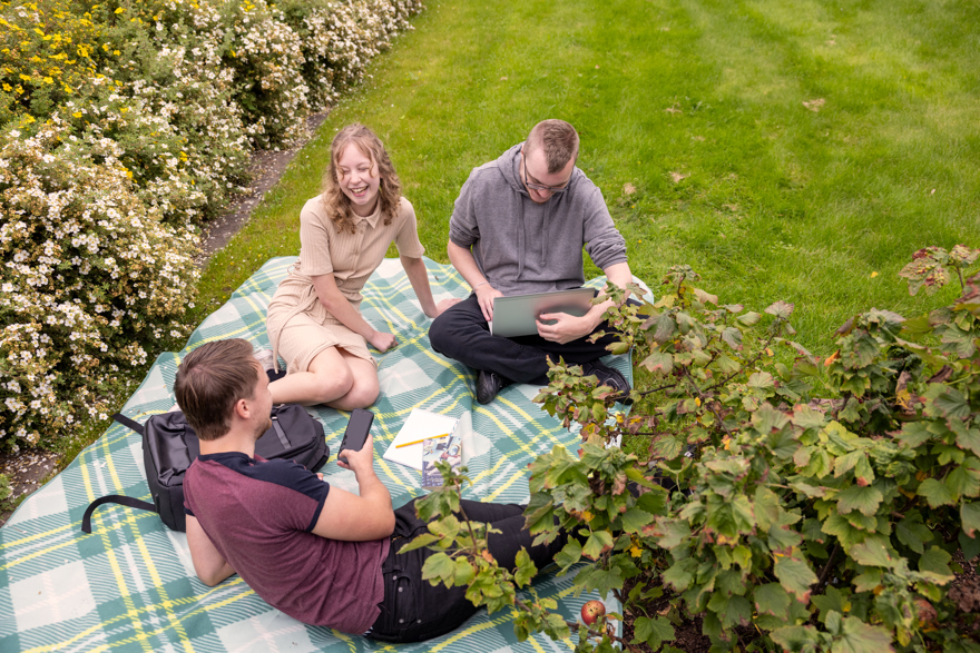 Tre deltagare sitter på en picknick-filt i gräset