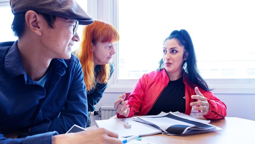 Två deltagare och en pedagog i samtal runt ett bord.